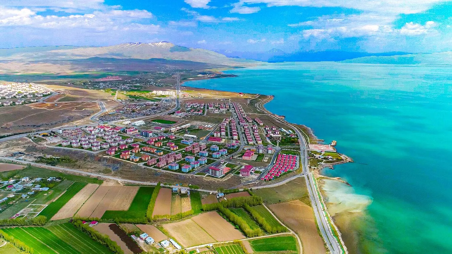 Turkuaz göl kıyısındaki konutları, tarlaları ve ağaçları gösteren havadan görünüm