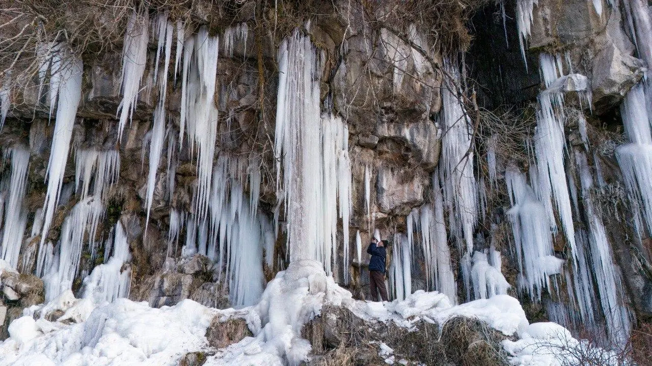 Koçköprü Kanyonu’nun kaya yüzlerinden sarkan uzun buz perdeleri, kar ve kayalıkların önünde fotoğraf çeken bir kişi.