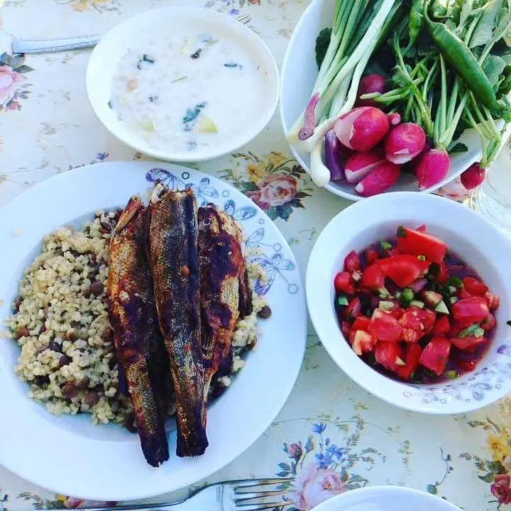 Pilav üzerinde pişmiş balıklar; yanında ayran aşı, domatesli salata, turp ve taze soğan.